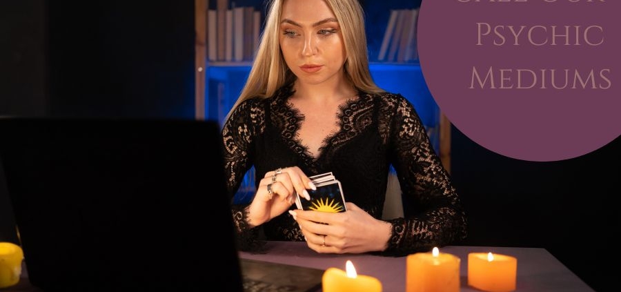 Women holding tarot cards surrounded by candles whilst at a computer