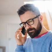 A male man with a beard and glasses, with dark hair on the phone to a psychic reader