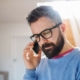 A male man with a beard and glasses, with dark hair on the phone to a psychic reader