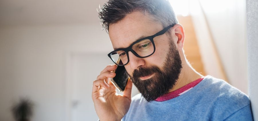 A male man with a beard and glasses, with dark hair on the phone to a psychic reader